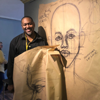 Steve Prince holds a piece of artwork with another behind him on a wall