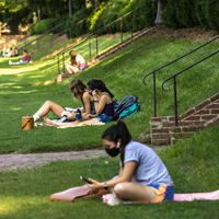 People wearing masks sit in a large grassy area