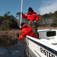 Two people in a boat take a sample from a body of water