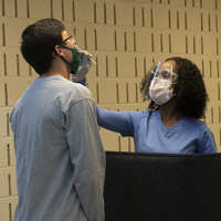 A person in scrubs takes a nasal swab from another person