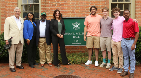 A number of people stand near a green, outdoor sign that says Hulon L. Willis Sr. Hall