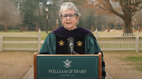 Jayne Barnard wears academic regalia and speaks from behind a podium outside
