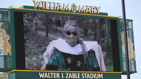 A person wearing a mask is shown on a large screen