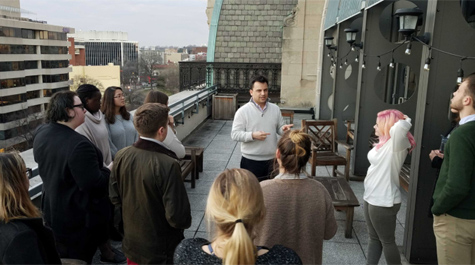 A person speaks to a group gathered on a balcony