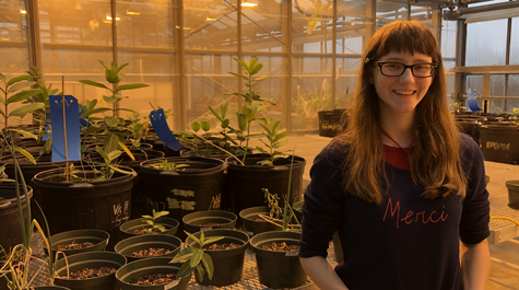 A person stands in a green house with plants behind them
