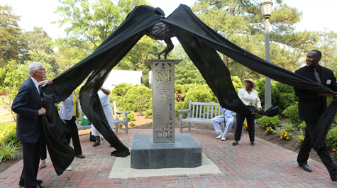 People pull down sheets covering a sculpture