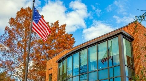 A flag pole with an American flag outside of a brick building with large windows