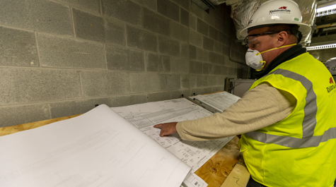 A person in a hard hat points at a sketch of a building