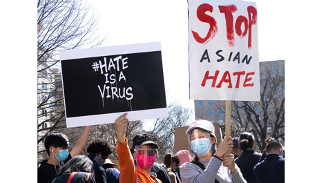 Two people hold up signs that say Hate is a Virus and Stop Asian Hate
