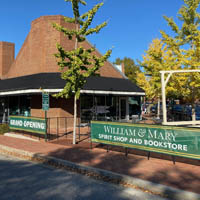 A brick building on a street corner with signs on the fence that say grand opening and W&M spirit shop and bookstore 