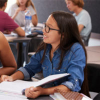 Teacher at table with books and a student sitting on each side