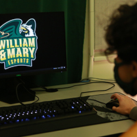 A masked student sits in front of a desktop computer 