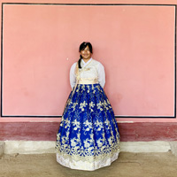 A person in a full, bright purple skirt stands against a pink wall