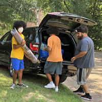 People wearing masks unload a van and stack items on the ground
