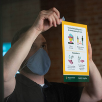 A person wearing a mask puts a sign up in a window that says people in the building must wear masks and wash hands 
