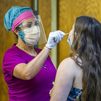 A person wearing PPE tests a student for COVID-19