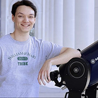 Student wearing W&M shirt leans against a telescope