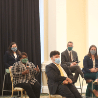 Five seated panelists with Marjorie Thomas on left with microphone