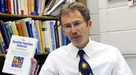 Joseph Galano: The professor holds a copy of his book, The Healthy Families America Initiative, which has helped him be recognized as a pioneer in research related to adverse childhood experiences (ACEs).