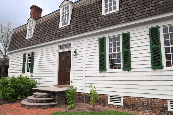 The Travis House exterior displays white siding, green window shutters, and a brick pathway with steps leading to the front door.