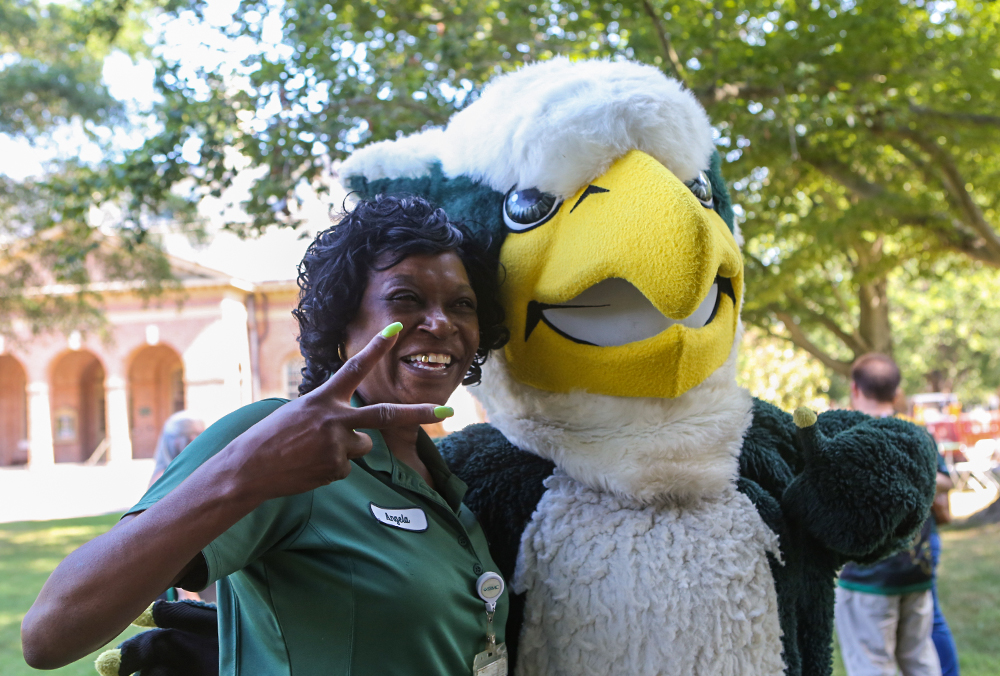 A William & 玛丽 employee holds up a peace sign while standing next to Griffin, the W&M mascot.