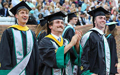 A group of Tribe athletes in Commencement attire smile and cheer as they enter Zable Stadium for the Commencement ceremony