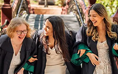 Three laughing graduates on the Crim Dell bridge during the Walk Across Campus