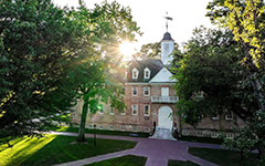 Aerial view of the historic Wren Building through lush trees with a sun glinting overhead
